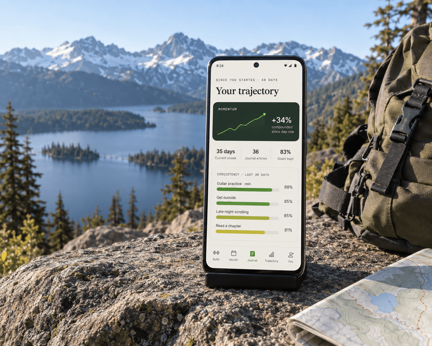Trajectory progress screen on a phone stand beside a hiking pack, overlooking a mountain lake